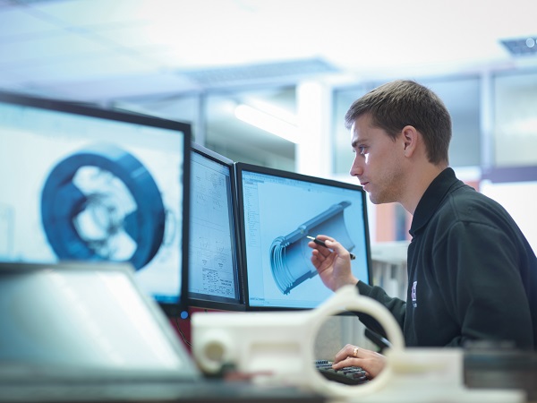 A mechanical engineer is sitting in front of a PC. You can see that he is designing machine parts with the help of a computer programme.