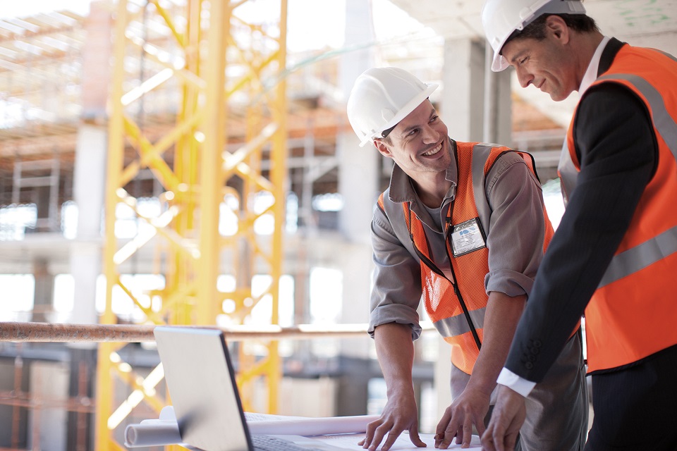 Two colleagues are standing on the building site looking at construction plans