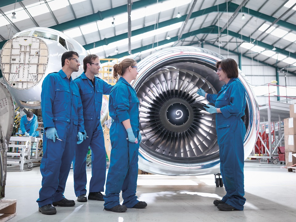 Mechanics stand in an airplane hangar and discuss