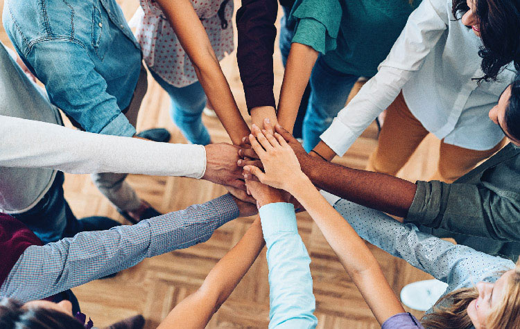 Share your Network 10 Mitarbeitende stehen im Kreis und haben ihre Händer in der Mitte aufeinander gelegt