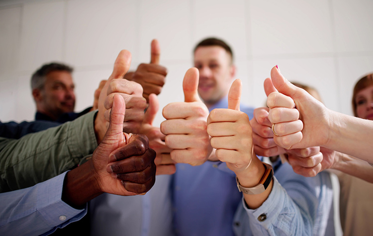 9 Mitarbeitende halten ihre Hand mit Daumen nach oben in die Mitte