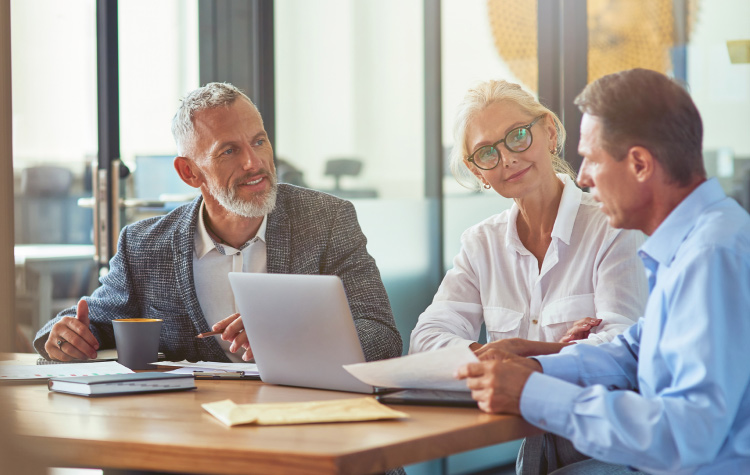 3 Mitarbeitende sitzen am Schreibtisch und haben ein Meeting