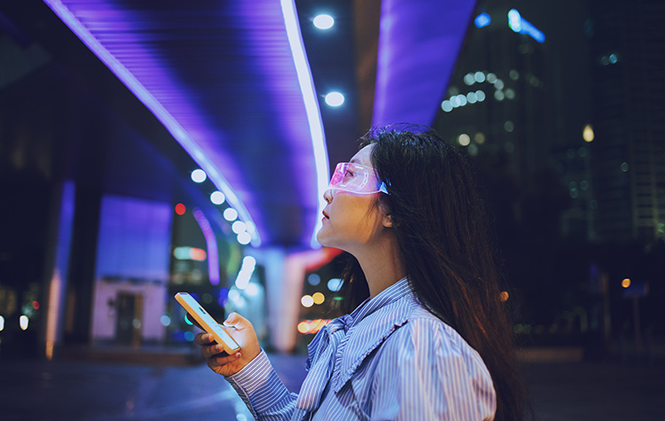 Innovatives Workforce Management Junge Frau steht mit futuristischer Brille in der Stadt und schaut auf ihr Handy