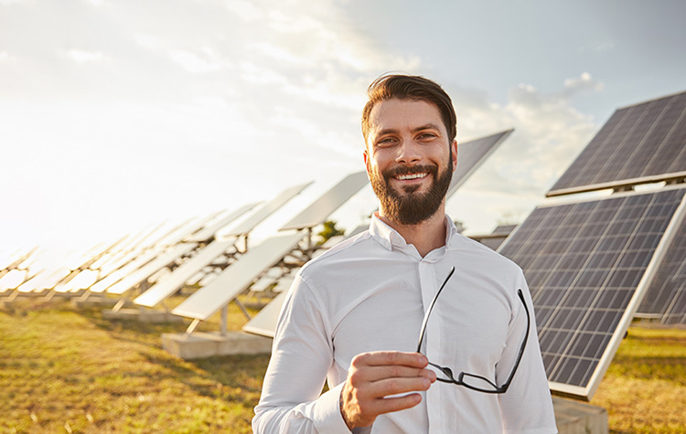 Mann steht auf einem Feld in der Sonne vor Solar-Panelen