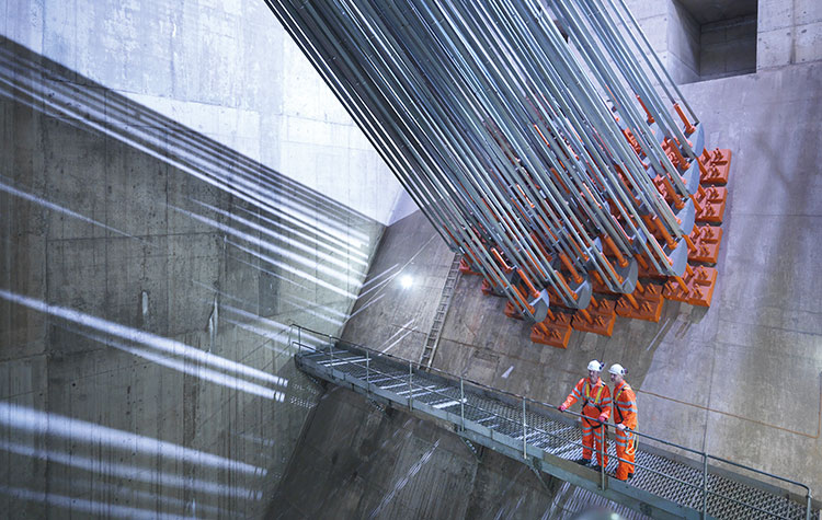 Two engineers stand in front of anchored steel cables in a huge plant