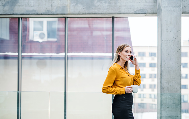 Junge Frau telefoniert mit einem Kaffee in der Hand