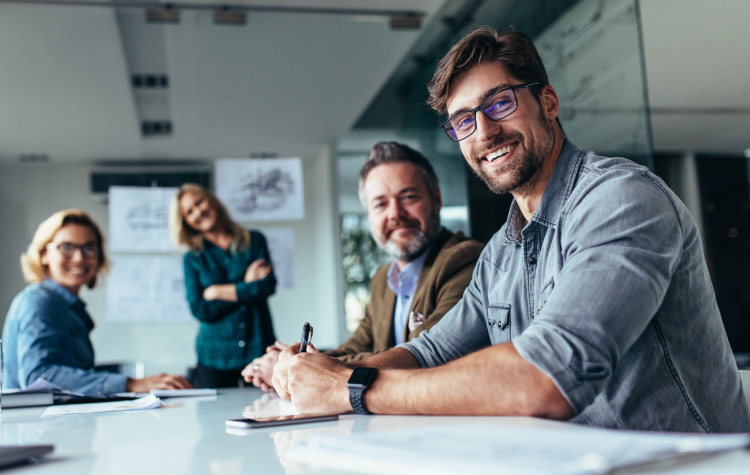 Mitarbeitende sitzen im Büro in einem Meeting, schauen aber in die Kamera