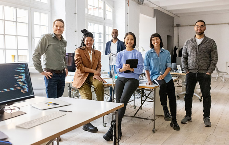Diverse Mitarbeitende stehen in einem Großraumbüro für ein Gruppenfoto