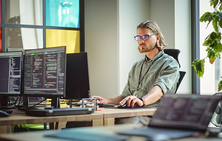 Programmierer sitzt im Büro vor Bildschirmen mit Code