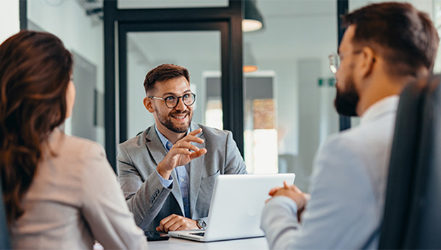 3 Mitarbeitende unterhalten sich an einem Schreibtisch im Büro