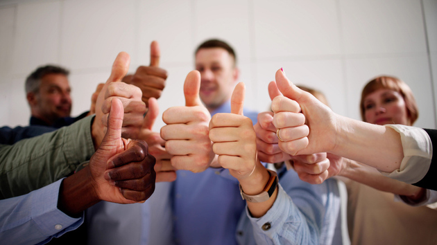 Mitarbeitende halten ihre Hände mit Daumen hoch in die Mitte