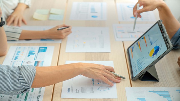 Hände auf einem Meetingtisch mit Projektunterlagen und einem Tablet