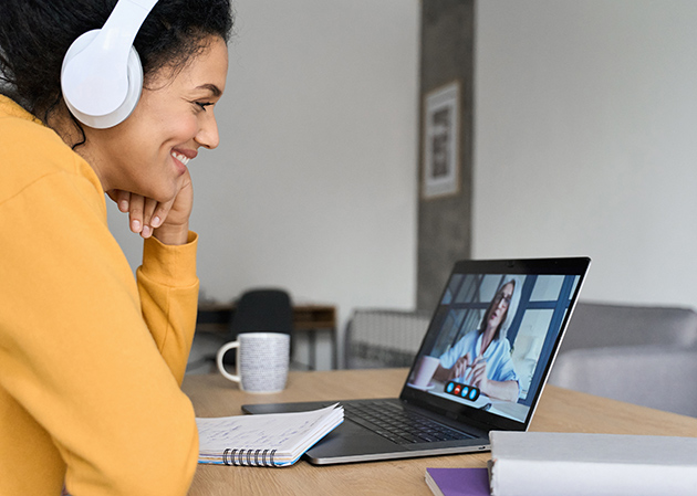 Foto im Home Office: Junge Frau sitzt vor ihrem Laptop und hält ein Video-Telefonat mit einer anderen Frau.